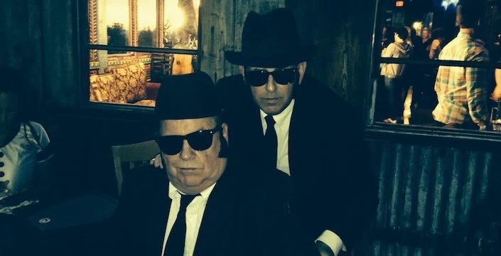 Two men in suits and hats are sitting at a table.