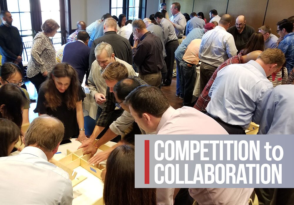 A group of people stand around tables working together on a team activity; text overlay reads "COMPETITION to COLLABORATION.