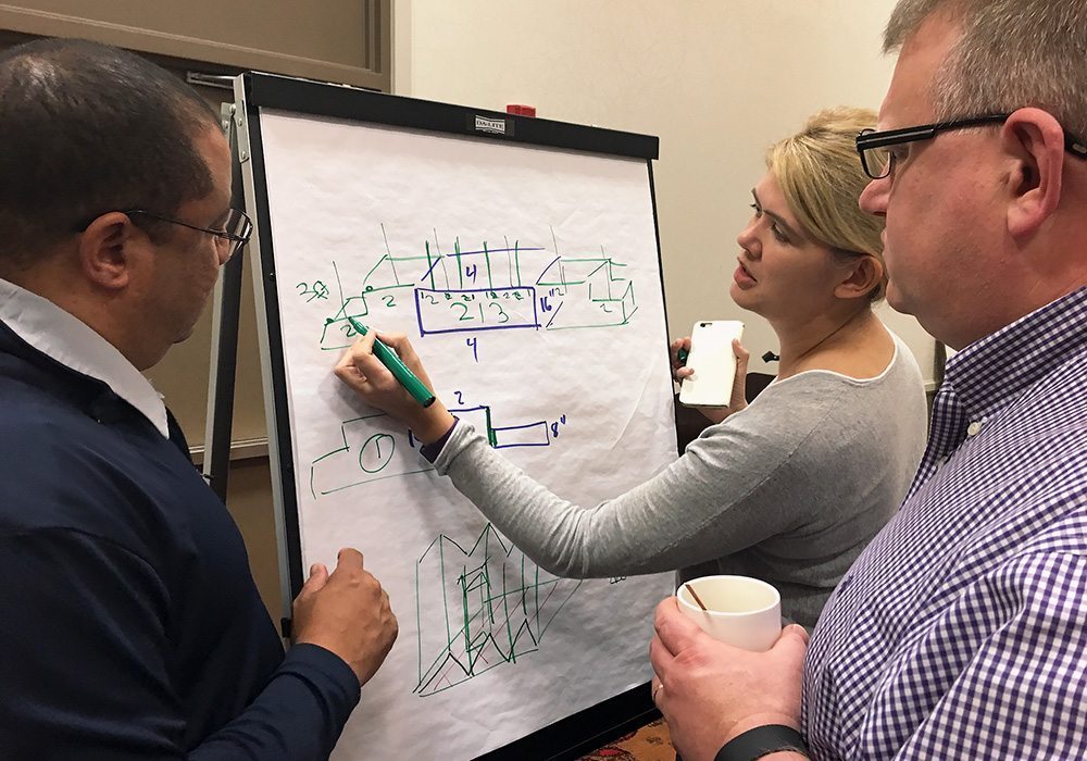 A group of people standing around a whiteboard with drawings on it.