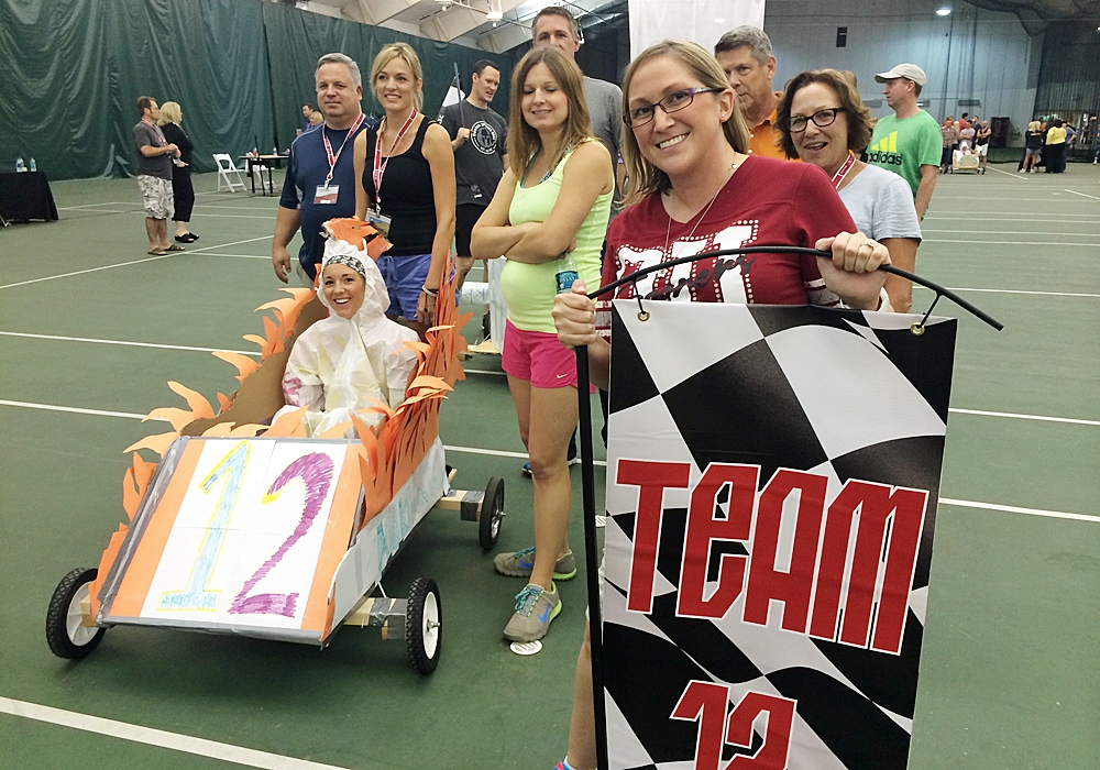 A group of people posing with a cardboard car on a court.