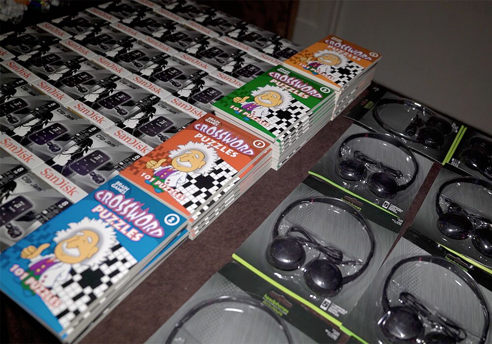 A table displays stacks of crossword puzzle books, USB drives in packaging, and boxed pairs of headphones.