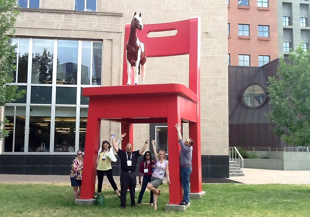 A group of people posing in front of a large red chair.