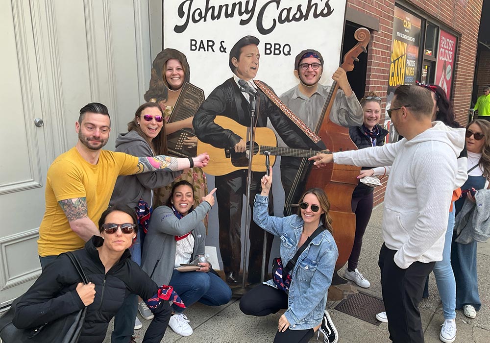 Group of people posing and smiling with a mural of johnny cash in the background.