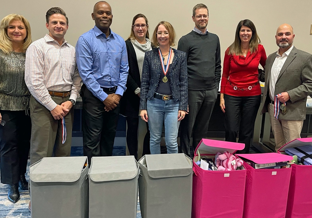 A group of people standing in front of pink bins for a toy donation drive.