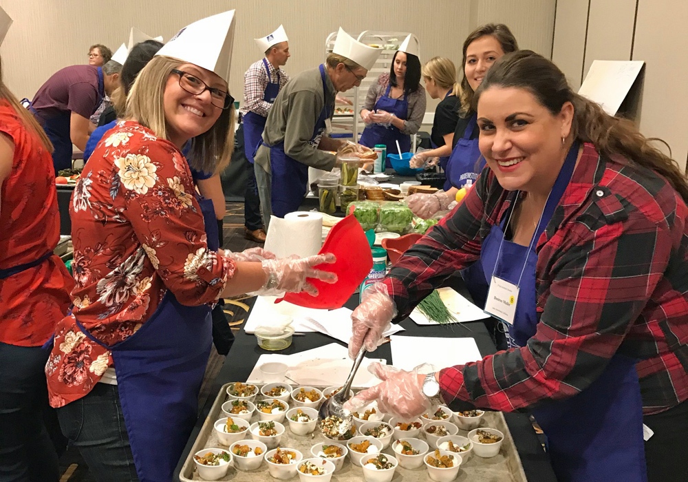 Two women in aprons are preparing food at a convention.