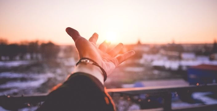 A person's hand reaching out to the sun.