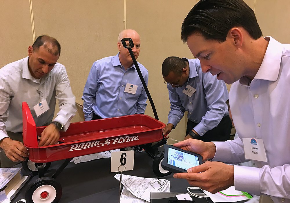 A group of men looking at a red wagon on a table.