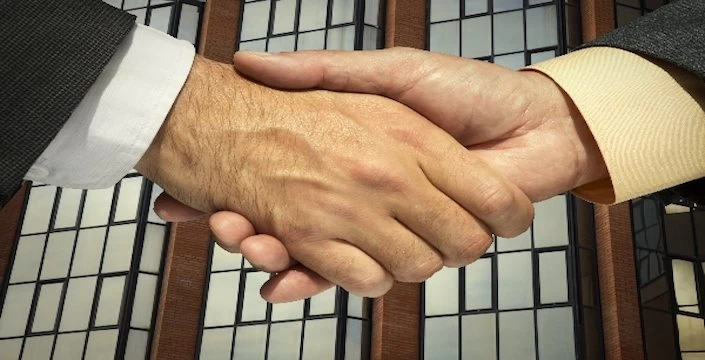 Two businessmen shaking hands in front of a building, showcasing their professional connection on LinkedIn.
