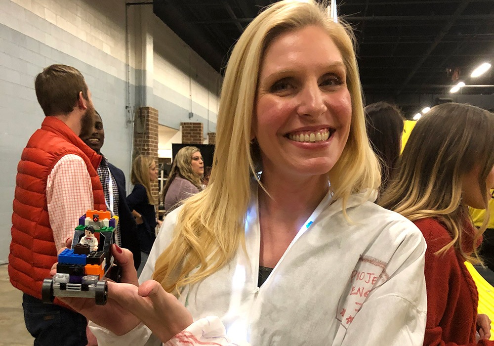A woman holding a lego robot in front of a crowd.
