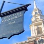 A boston common sign with a clock tower in the background.