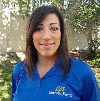 A woman in a blue polo shirt standing in front of a tree.