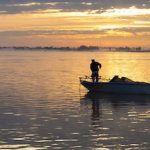 A man in a boat on the water at sunset.