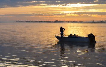 A man in a boat on the water at sunset.