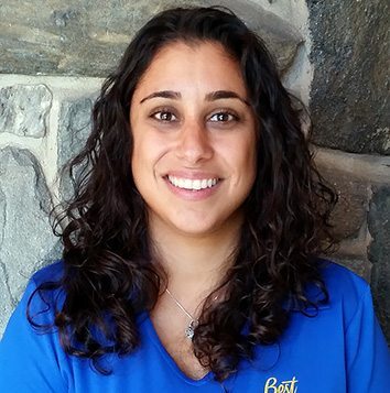 A woman in a blue shirt smiling in front of a stone wall.