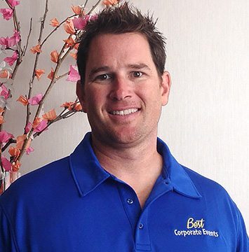 A man in a blue shirt standing in front of flowers.