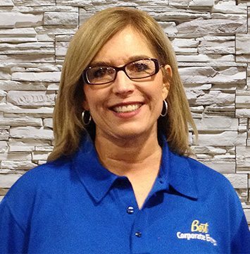 A woman in a blue polo shirt standing in front of a stone wall.