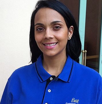 A woman in a blue shirt smiling in front of a building.