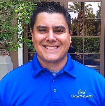 A man in a blue shirt smiling in front of a palm tree.