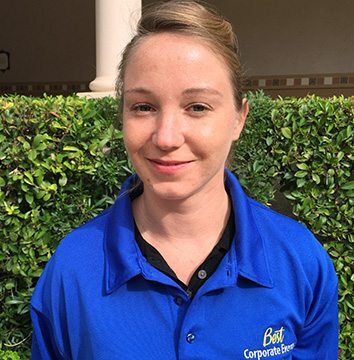 A woman in a blue shirt standing in front of bushes.