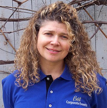 A woman in a blue shirt standing in front of a fence.