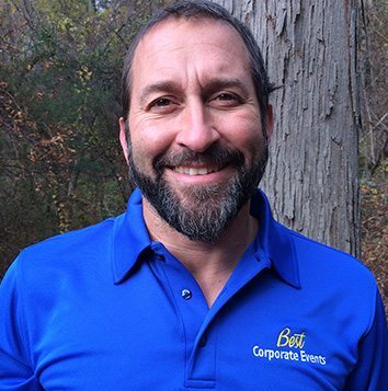 A man in a blue shirt smiling in front of a tree.