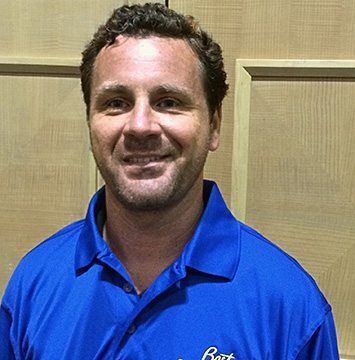 A man in a blue shirt smiling in front of a wall.