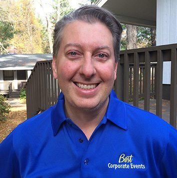A man in a blue shirt smiling in front of a house.
