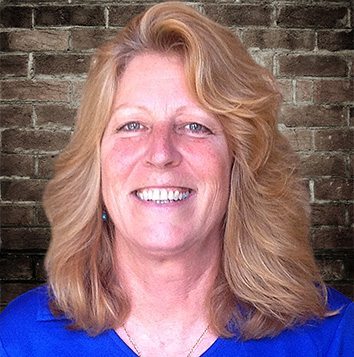 A woman smiling in front of a brick wall.