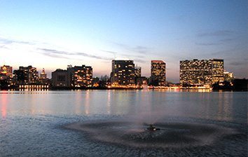 A city at dusk with a fountain in the middle of a lake.