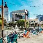 A group of people are sitting on a boardwalk in front of a city.