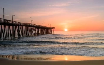 A pier in Virginia Beach with the sun setting behind it, providing a picturesque backdrop for team activities.