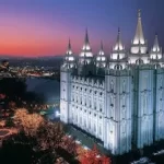 The salt lake temple is lit up at dusk in Utah.