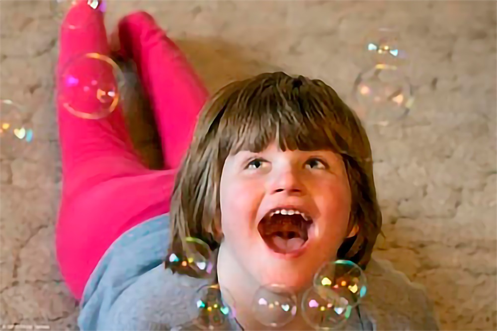 A young girl laying on the floor with soap bubbles.