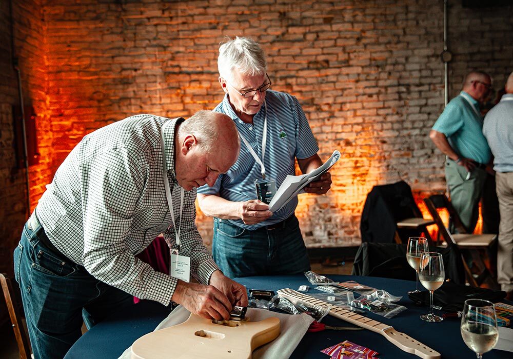 Two men working on a guitar at a table.