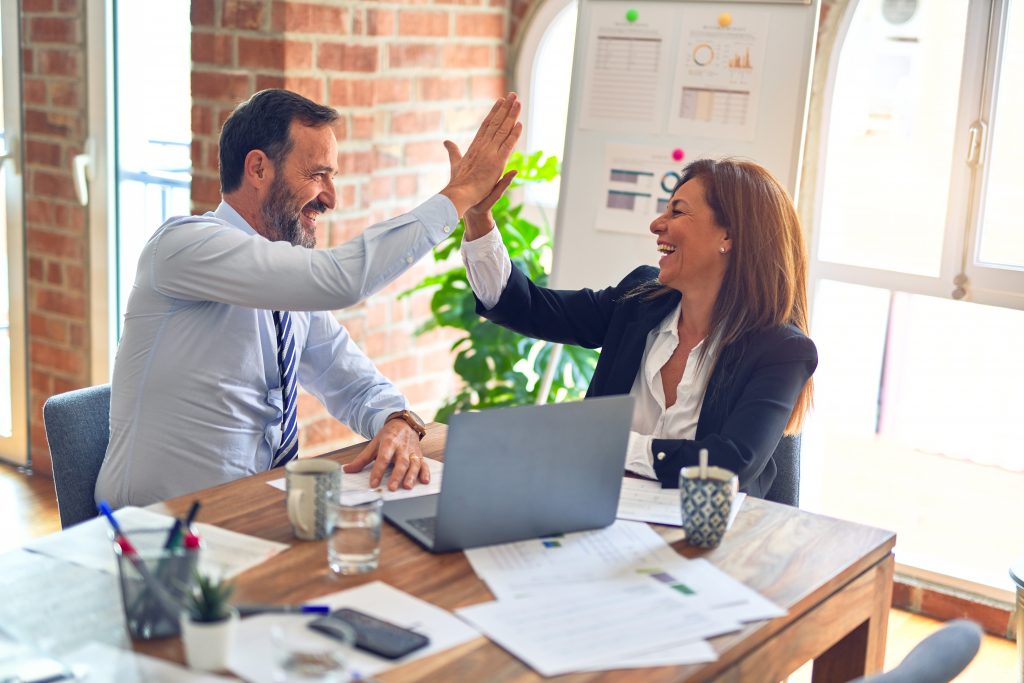Two business people giving each other high fives in an office.