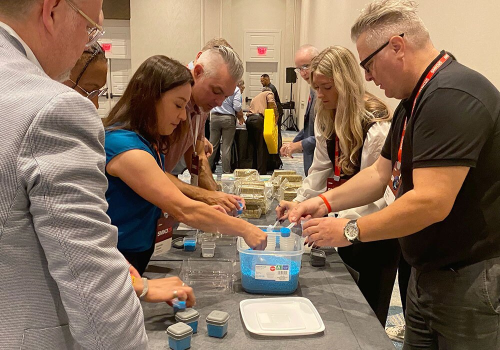 People gathered around a table, participating in a group activity focused on hydroponics, utilizing blue materials and containers to cultivate plants.