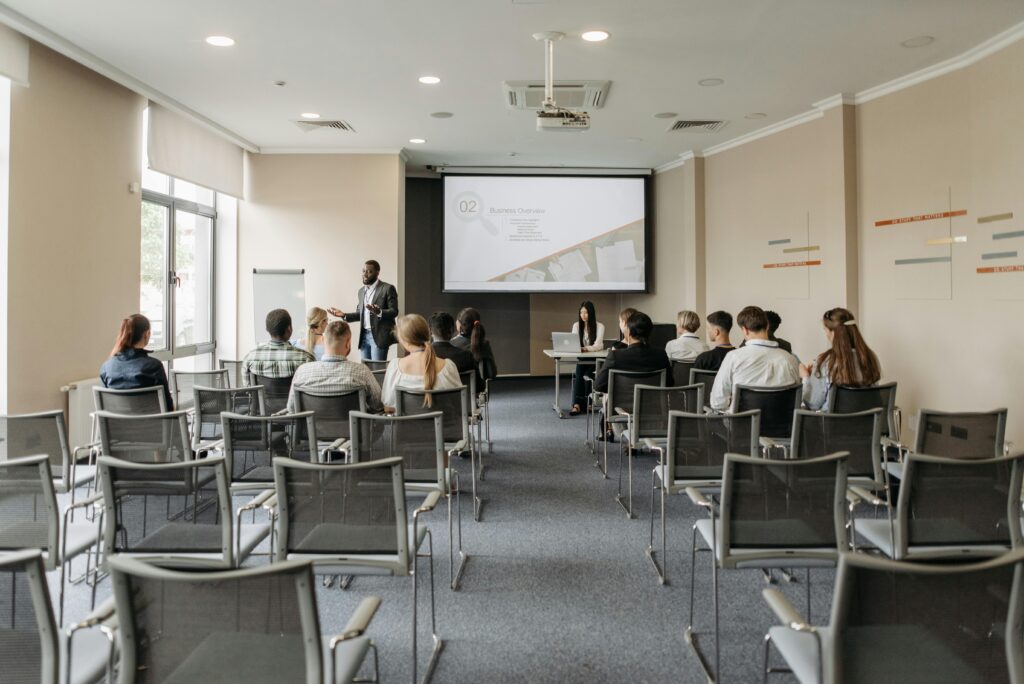 A man presents to a small audience in a modern conference room, sharing a business overview slide that highlights the importance of team building and training.