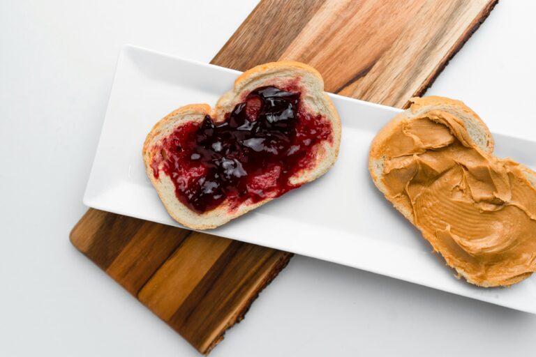 Two slices of bread on a rectangular white plate—one with peanut butter, the other with grape jelly—demonstrate how combining training and team building can create something even better together, arranged neatly on a wooden board.