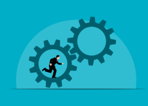 A person in a business suit running inside a large gear, embodying learning by doing, with another large gear nearby on a blue background.