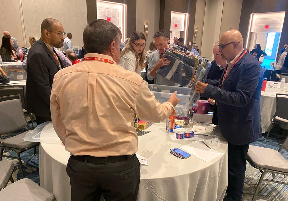 People gathered around a table, assembling items into plastic containers in a conference room setting.