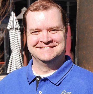 A man in a blue shirt smiles in front of a restaurant.