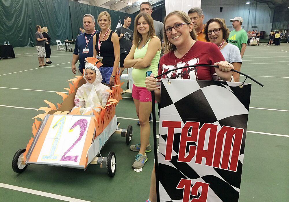 A group of people posing with a cardboard car on a court.