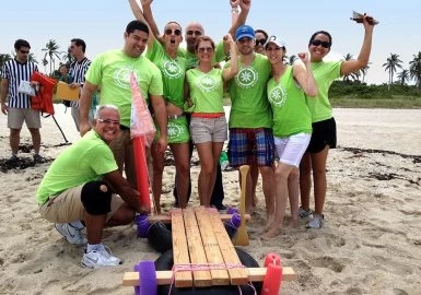 A group of people posing with a wooden boat on the beach.