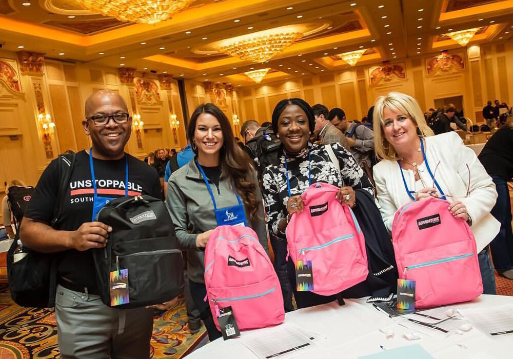 Four people posing with backpacks at a convention.