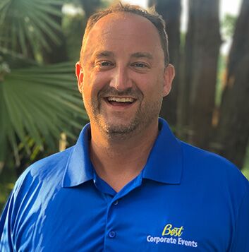 A man in a blue shirt smiling in front of palm trees.