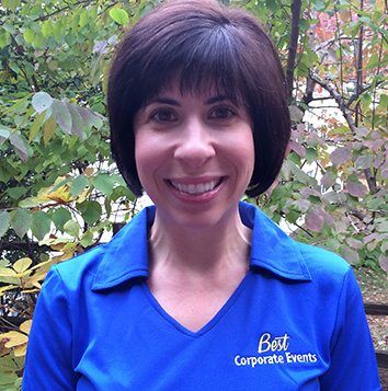 A woman in a blue shirt smiling in front of trees.
