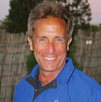 A man in a blue shirt smiling in front of a fence.