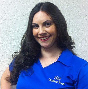 A woman in a blue shirt smiling in front of a wall.
