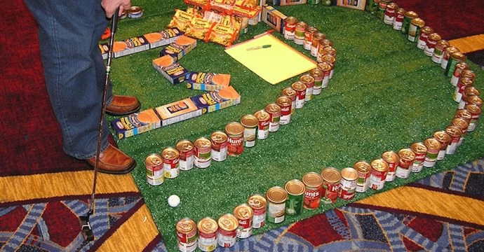 A man is standing next to a large pile of cans at a mini-golf course.