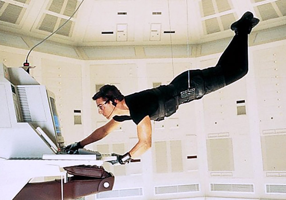 A man is hanging from a ceiling while using a computer.